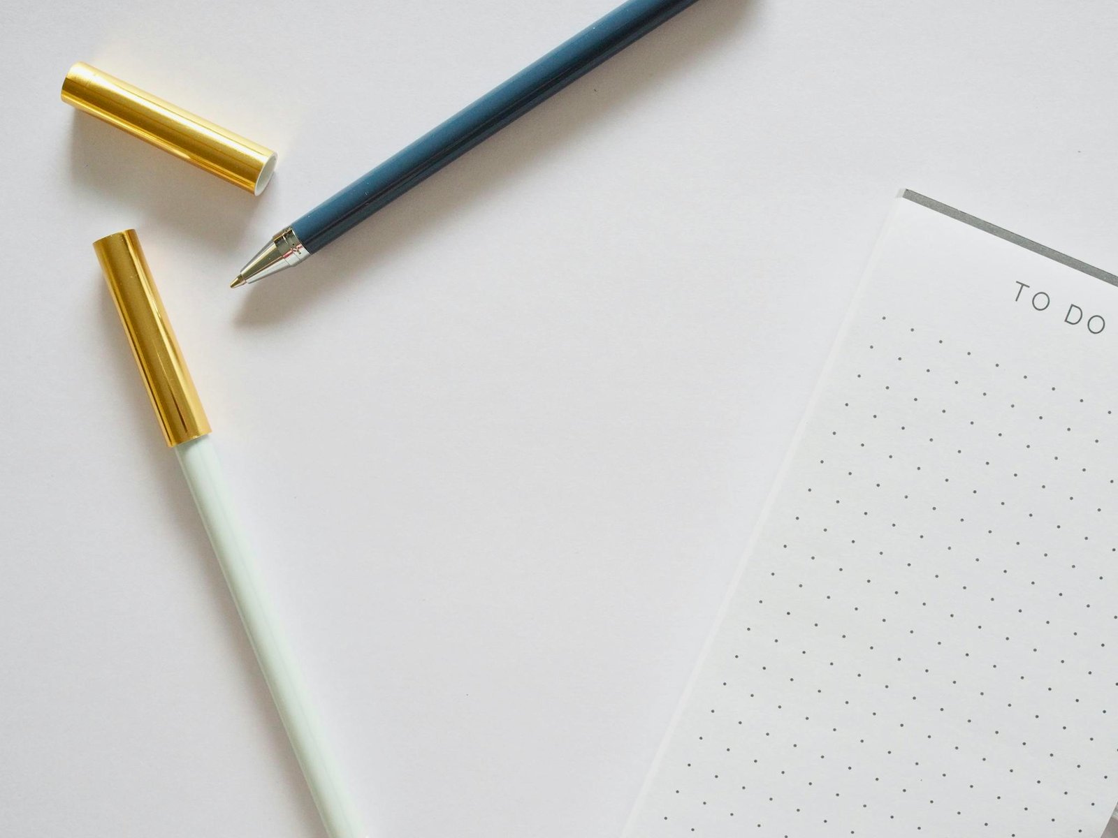 A minimalist flat lay featuring a to-do list notebook and pens on a white background.